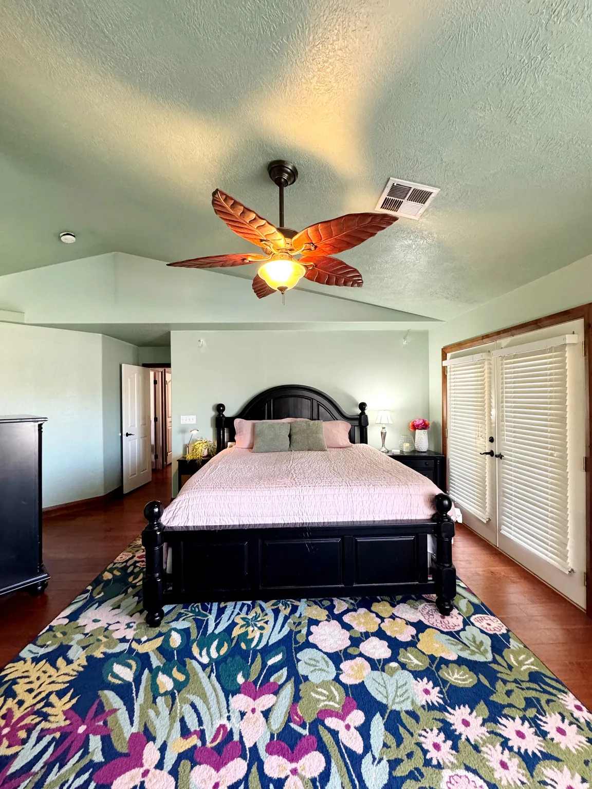 Vaulted ceiling with a ceiling fan, dual French doors with interior louvered shutters, and wood-finish flooring