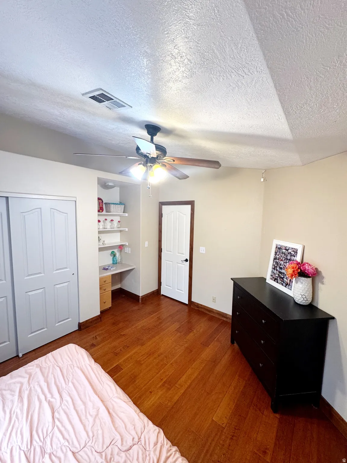 Wood-finish flooring with a ceiling fan light fixture, built-in desk, and bi-fold closet doors