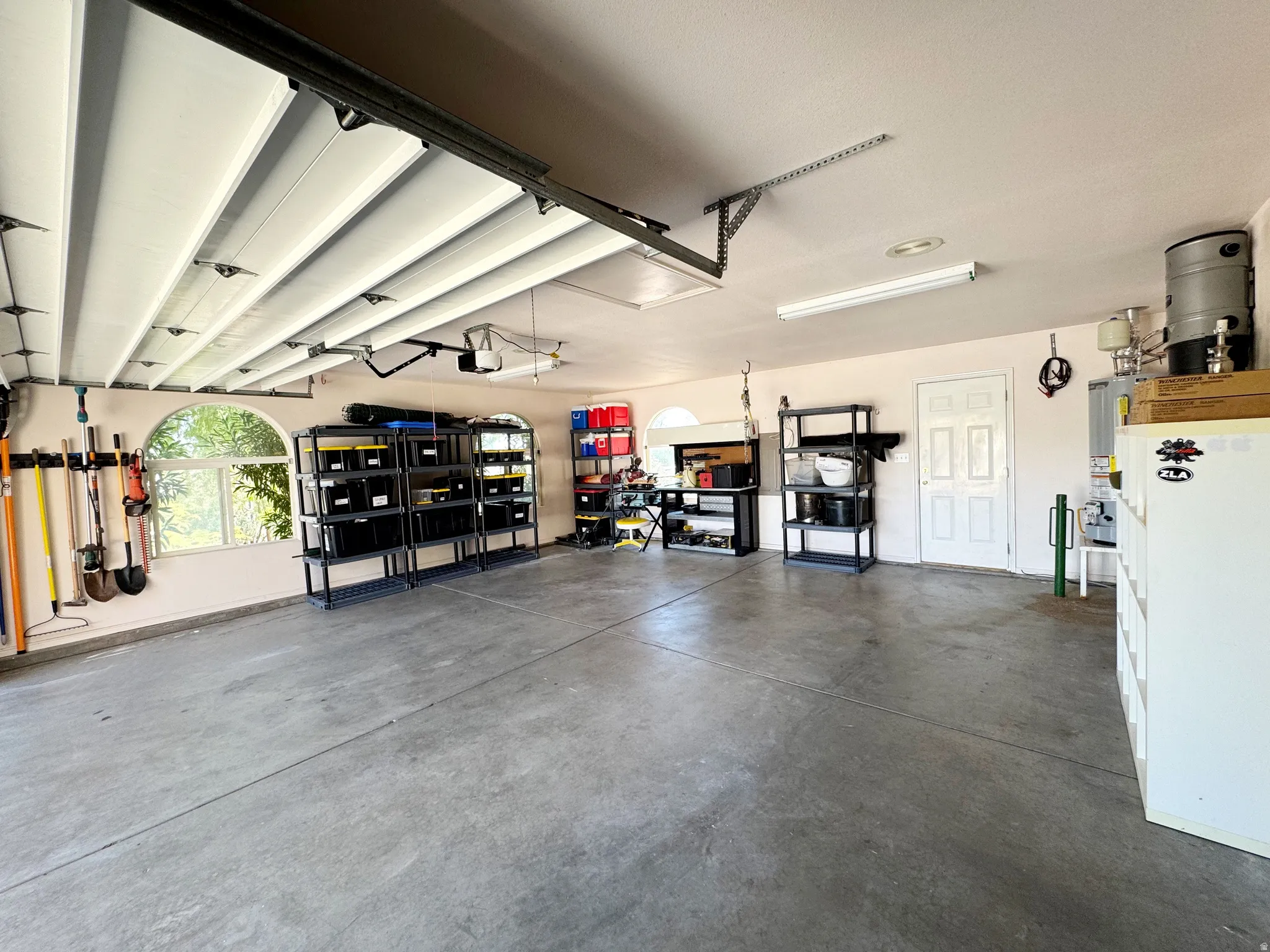Spacious garage with concrete flooring, arched windows, and white garage door panels