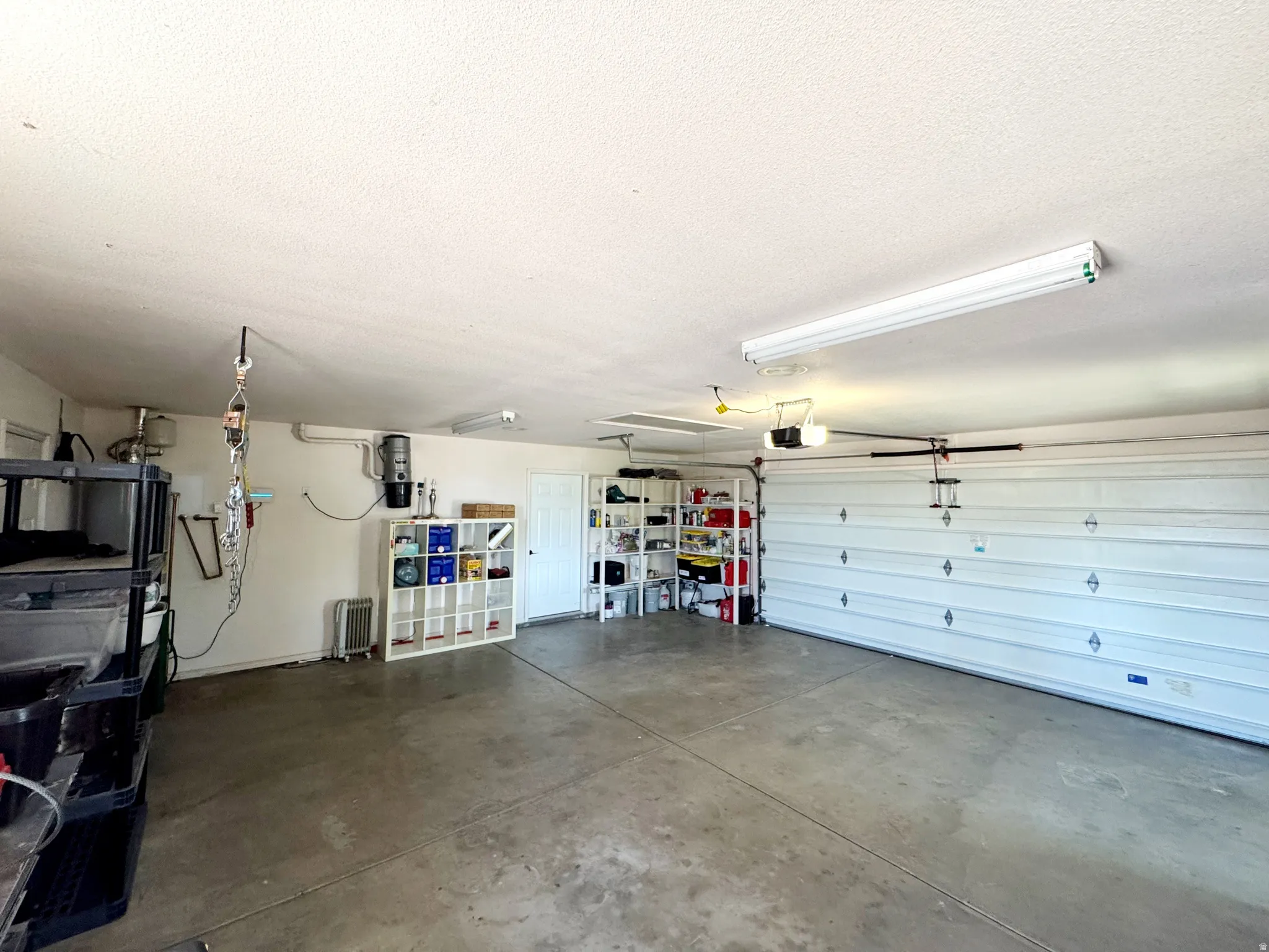 Spacious garage with concrete flooring, overhead fluorescent lighting, and a white paneled garage door