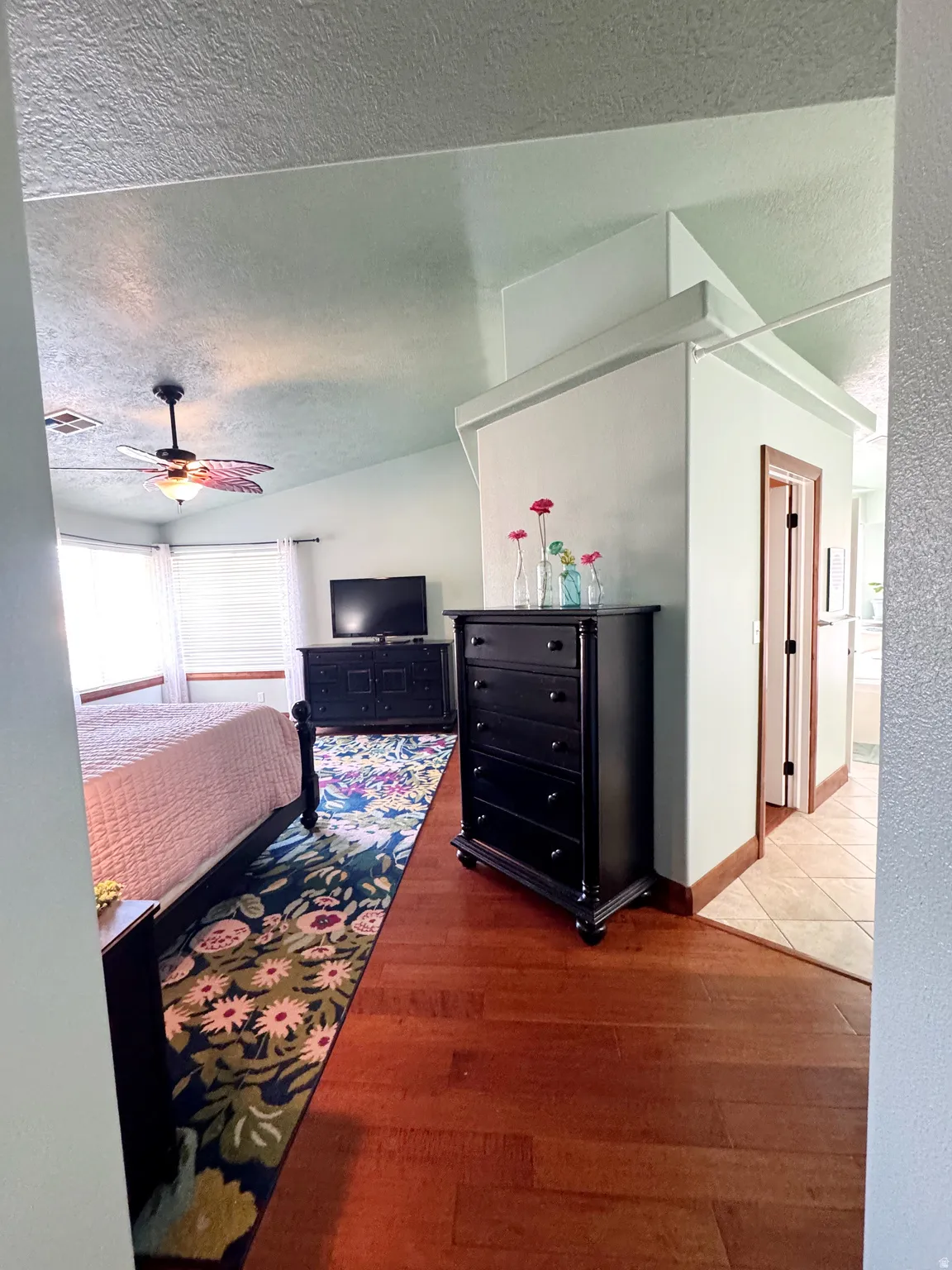 Vaulted ceiling with a ceiling fan, bay windows with window treatments, rich wood-finish flooring, and a dedicated alcove with tile flooring