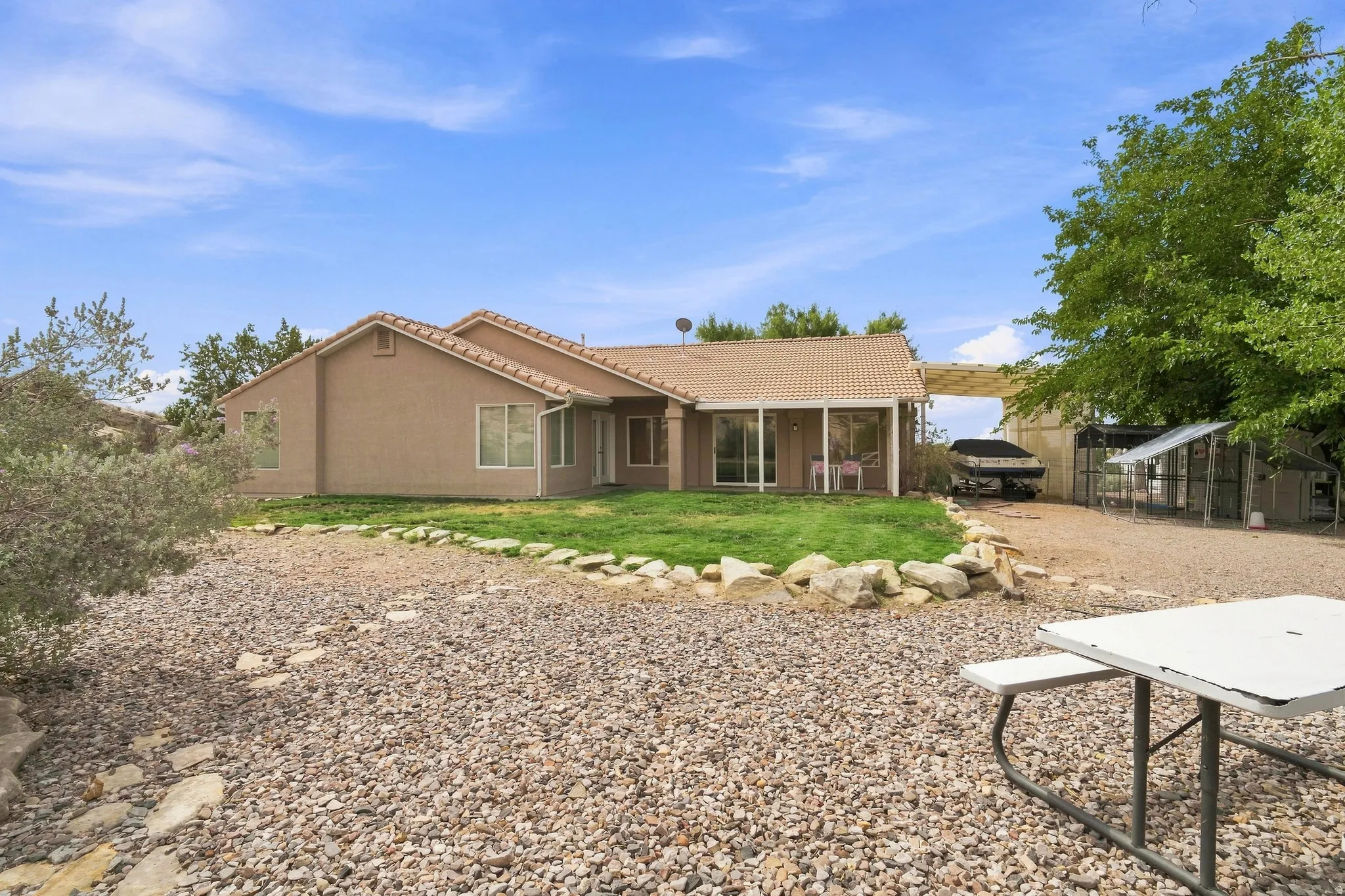 Stucco exterior with a tiled roof, covered patio, sliding glass doors, and expansive gravel landscaping