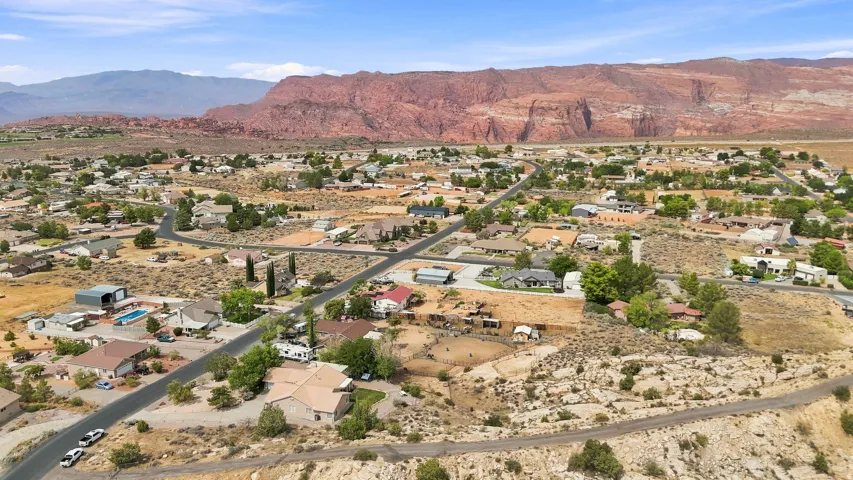 Expansive desert landscape with scattered residential properties, featuring paved roads and distant red rock formations