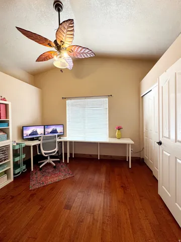 Vaulted ceiling with an attached ceiling fan, rich wood-finish flooring, and a window with blinds