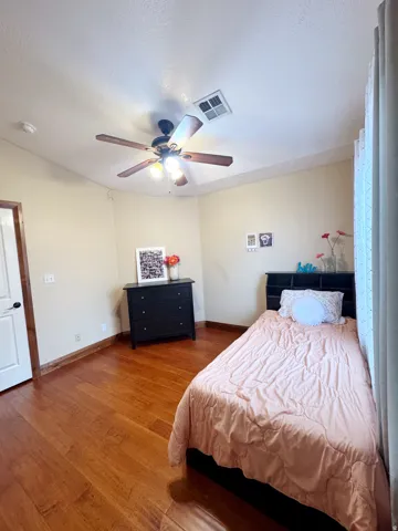 Wood-finish flooring, ceiling fan with integrated lighting, and a white interior door with dark hardware
