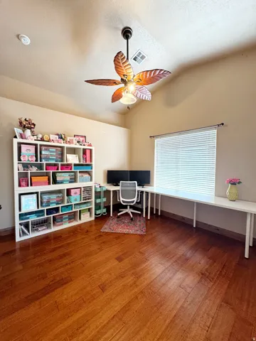 Vaulted ceiling with a decorative ceiling fan, wood-finish flooring, and a built-in L-shaped desk