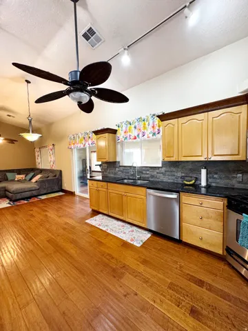 Hardwood flooring with a kitchen featuring wood cabinetry, dark countertops, and a stainless steel dishwasher
