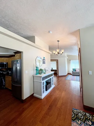 Hardwood flooring throughout, recessed ceiling details, kitchen with wood cabinetry, stainless steel refrigerator, and an overhead chandelier