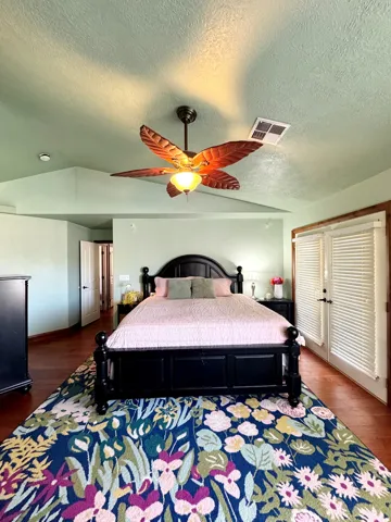 Vaulted ceiling with a ceiling fan, dual French doors with interior louvered shutters, and wood-finish flooring