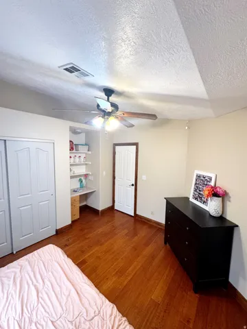 Wood-finish flooring with a ceiling fan light fixture, built-in desk, and bi-fold closet doors