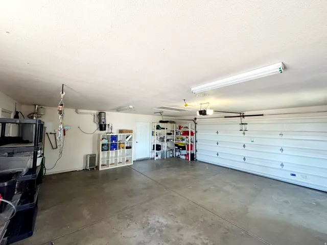 Spacious garage with concrete flooring, overhead fluorescent lighting, and a white paneled garage door
