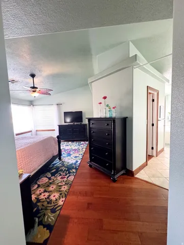 Vaulted ceiling with a ceiling fan, bay windows with window treatments, rich wood-finish flooring, and a dedicated alcove with tile flooring