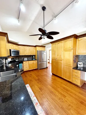 Kitchen featuring wood-finish flooring, light wood cabinetry, dark countertops, a double basin sink, and stainless steel appliances
