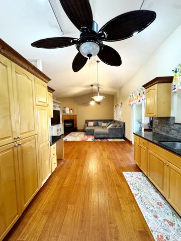 Wood-finish flooring throughout, light-toned cabinetry with hardware, dark countertops, and a ceiling fan with integrated lighting
