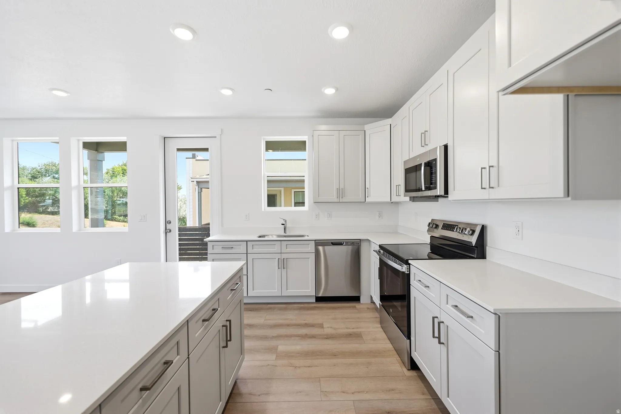 Kitchen featuring a large island with white countertops, stainless steel appliances, light wood-finish flooring, and recessed lighting