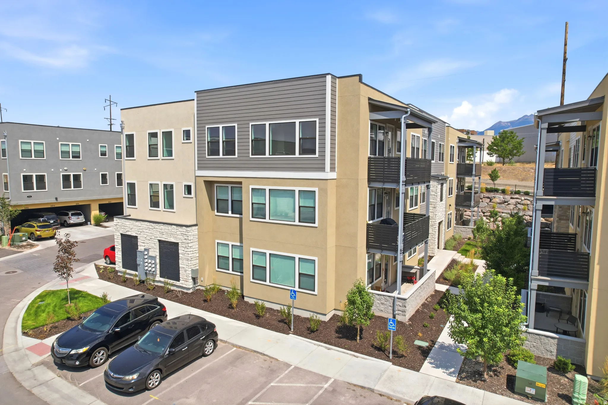 Multi-story building featuring contemporary architecture, multiple balconies, a mix of stucco and stone-finish siding, and integrated landscaping