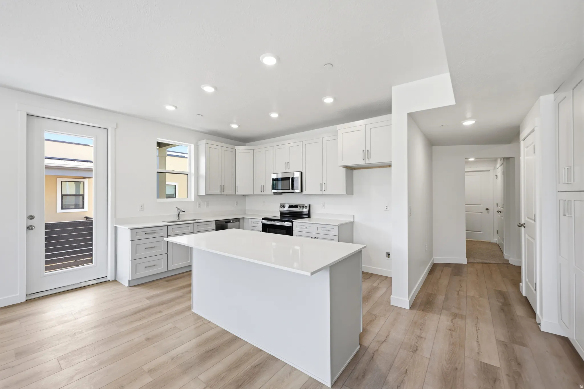 Contemporary kitchen featuring white cabinetry, a central island with a solid surface countertop, stainless steel appliances, and wood-finish flooring
