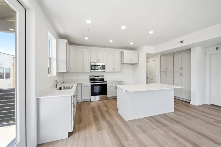 Modern kitchen featuring light cabinetry, stainless steel appliances, quartz countertops, a kitchen island, and wood-finish flooring