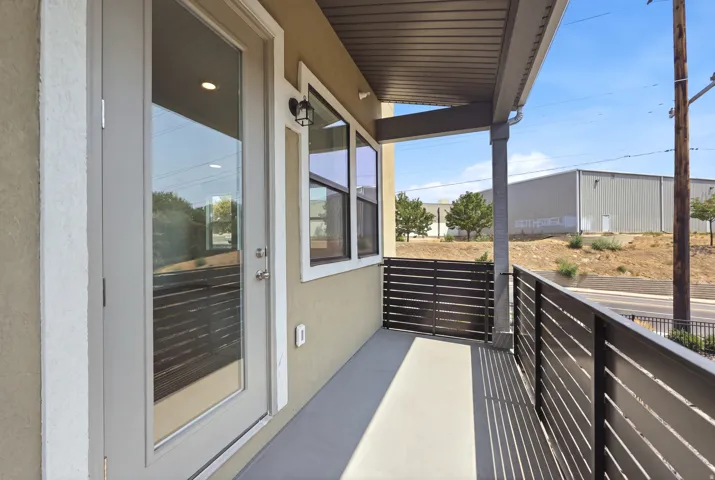 Covered balcony with a concrete surface, featuring horizontal slat railing and a glass-paneled door