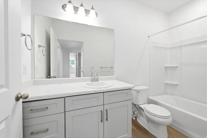 White bathroom featuring a vanity with a white countertop, undermount sink, and light gray cabinetry with brushed nickel hardware