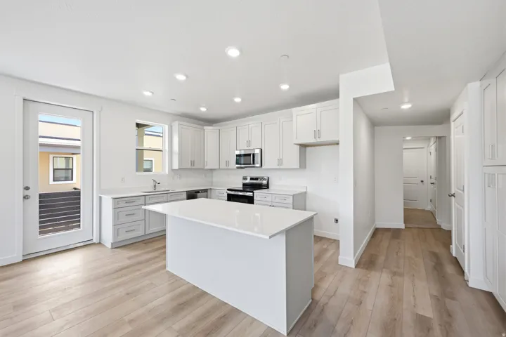 Contemporary kitchen featuring white cabinetry, a central island with a solid surface countertop, stainless steel appliances, and wood-finish flooring