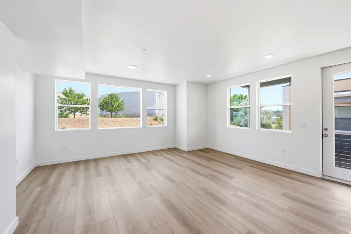 Spacious room featuring wood-finish flooring, white walls, multiple windows, recessed lighting, and a glass-paneled exterior door