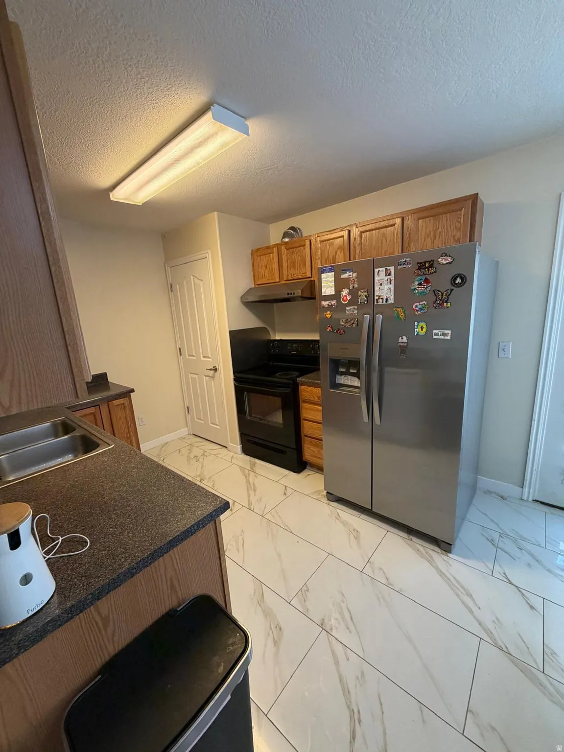 Kitchen featuring wood-finish cabinetry, stainless steel refrigerator, black range with matching hood, and a dual basin sink