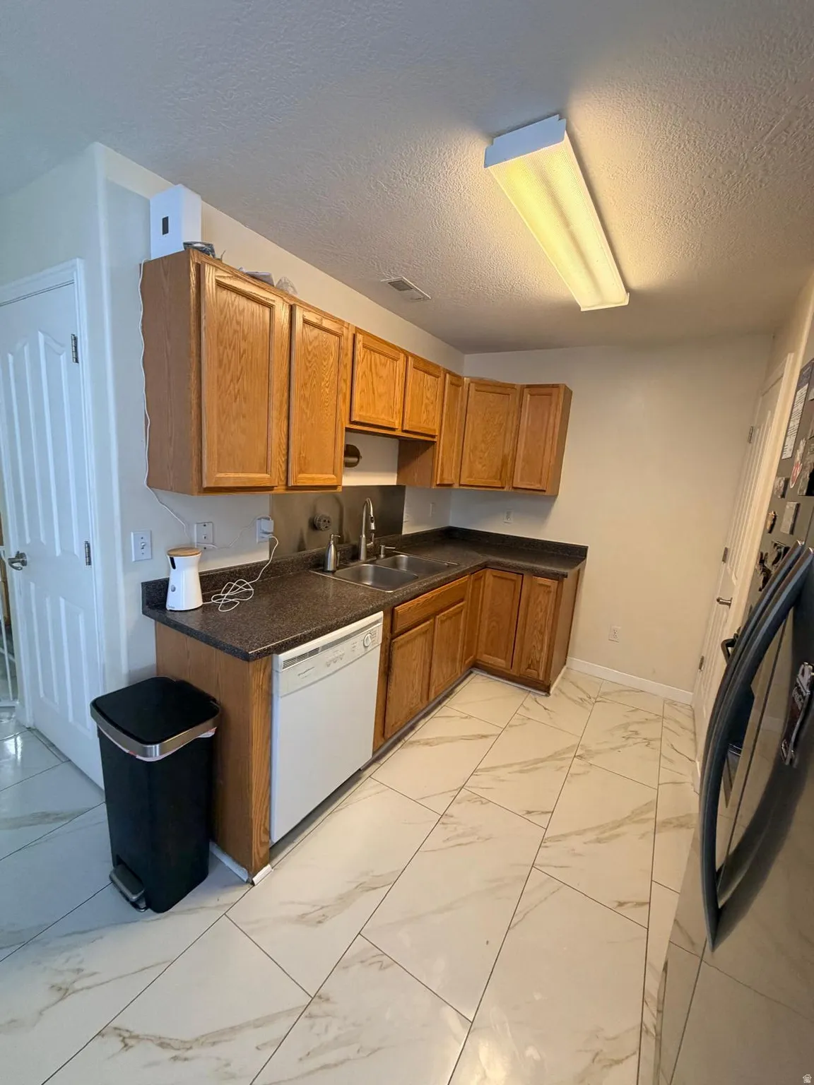 Kitchen featuring wood cabinetry, stone-look countertops, a stainless steel double basin sink, and tile flooring