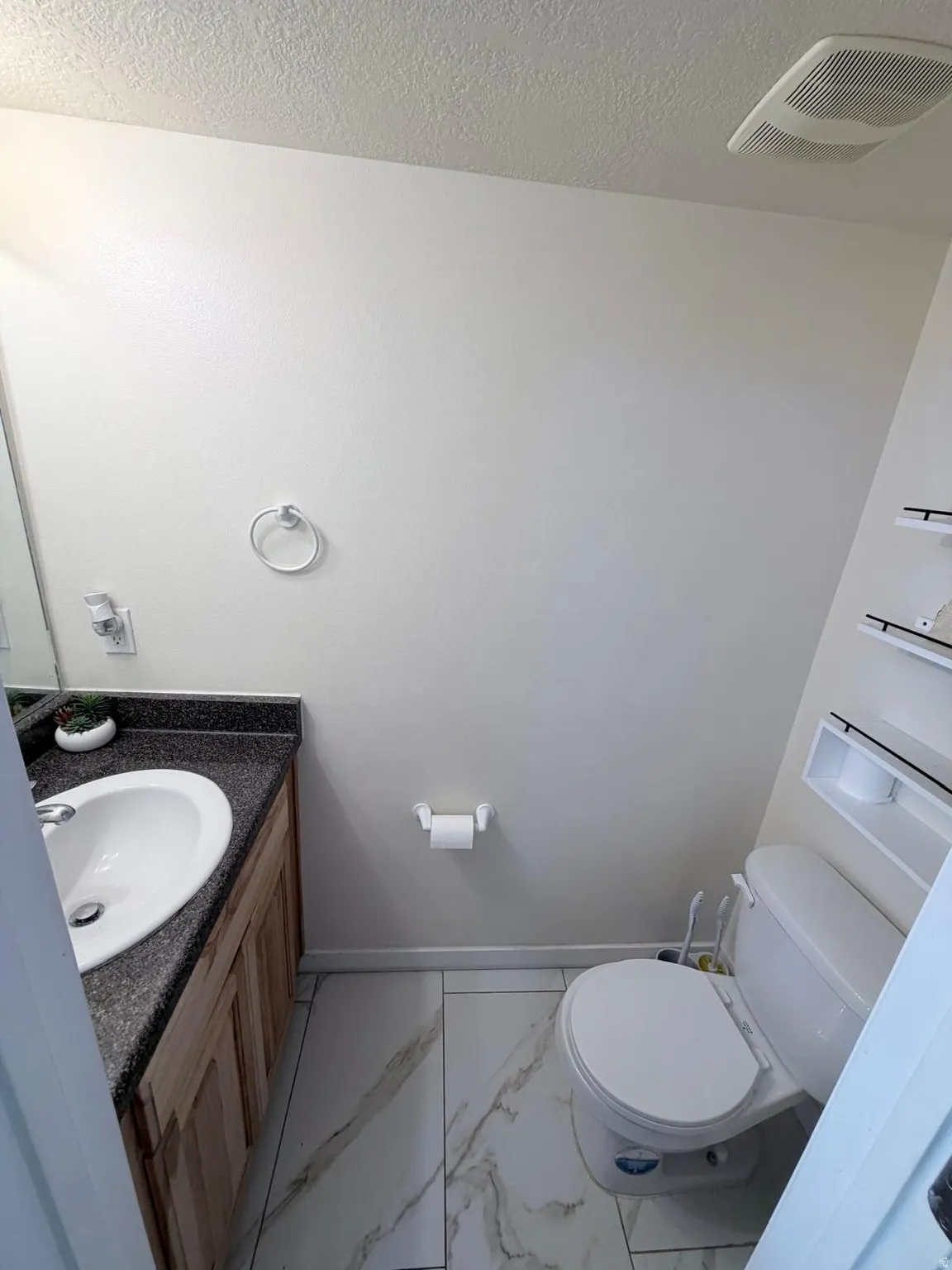 Vanity with an integral sink and dark speckled countertop, wood-finish cabinetry, and white tile flooring with veining