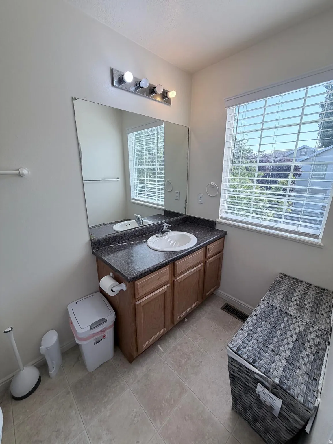 Tile flooring, single vanity with a white basin sink, dark countertop, wood-finish cabinetry, and a large mirror