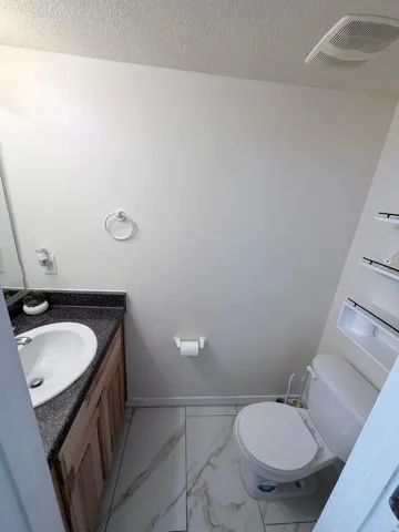 Vanity with an integral sink and dark speckled countertop, wood-finish cabinetry, and white tile flooring with veining