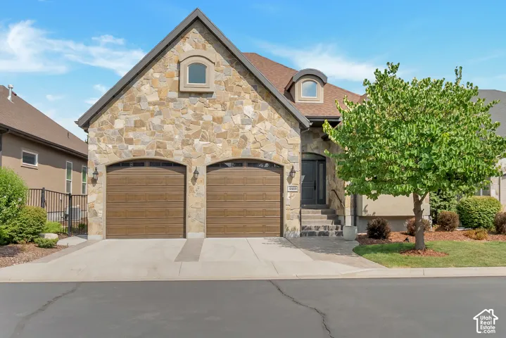 Stone veneer exterior, arched garage doors, dormer window, mature tree, concrete driveway