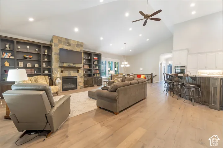 Vaulted ceiling with recessed lighting, stone-clad fireplace with mantel, built-in shelving, wood-finish flooring, and a kitchen island with seating
