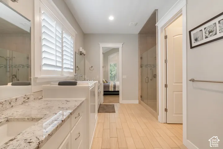 Double vanity with light-toned countertop, wood-finish flooring, glass-enclosed shower, and plantation shutters