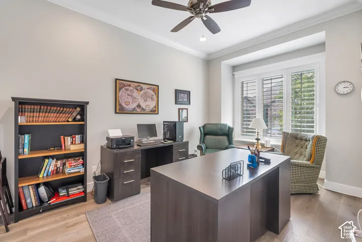 Home office with warm-toned wood-finish flooring, crown molding, and a bay window with plantation shutters