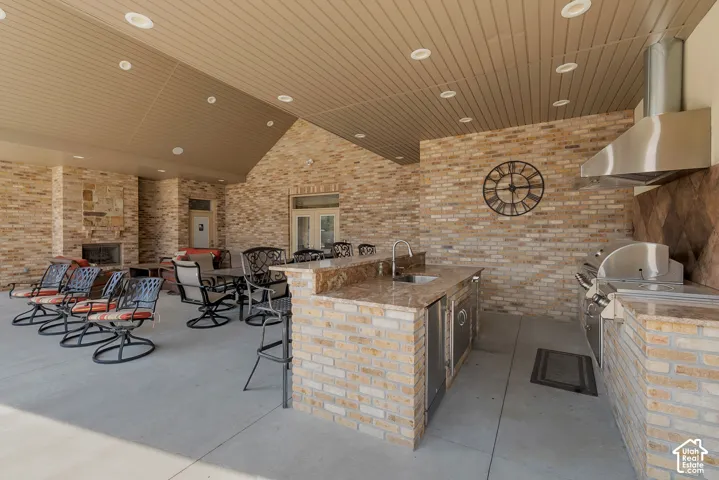 Covered outdoor living space featuring brick construction, a built-in outdoor kitchen with stainless steel appliances, a stone countertop, and a fireplace