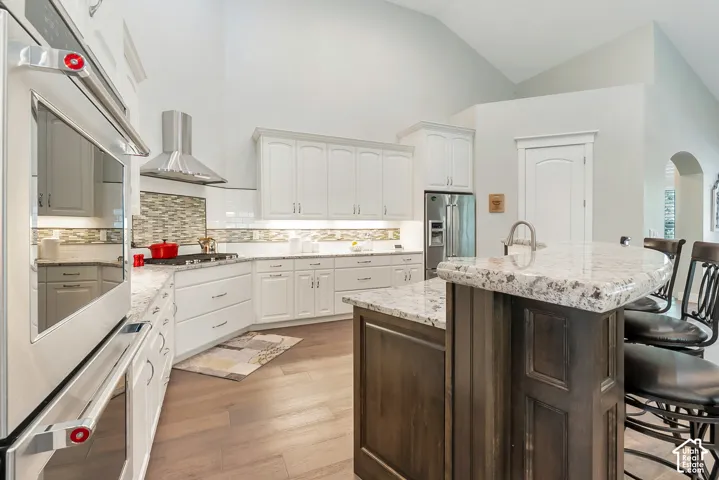 Kitchen featuring white cabinetry, stainless steel appliances, wood-finish flooring, and a central island with a light-toned granite countertop