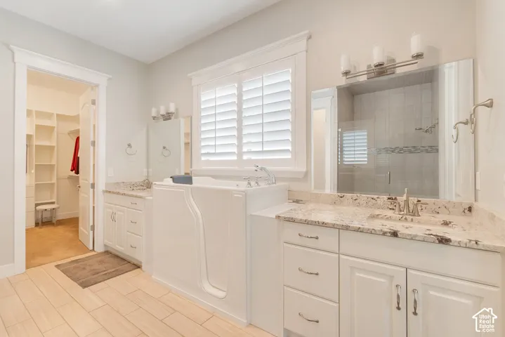 Dual vanity with integrated sinks, walk-in tub with chrome fixtures, and wood-finish flooring