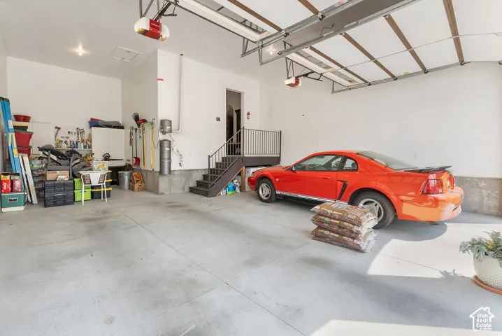 Attached garage with concrete flooring, white walls, and a built-in staircase with a black metal railing
