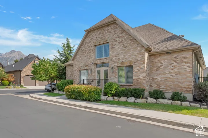 Brick exterior facade with gabled roofline, double entry doors, front landscaping with natural stone accents, and a clear mountain backdrop