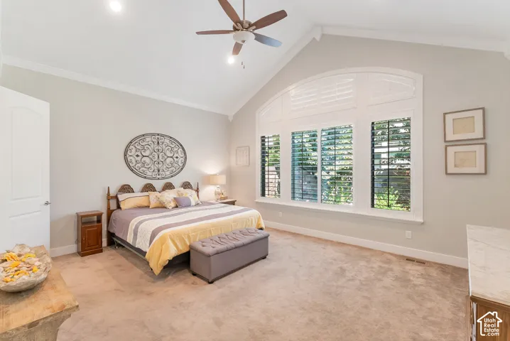 Master beedrom includes vaulted ceiling with a ceiling fan, arched transom window, three rectangular windows with plantation shutters, and light-toned carpet flooring