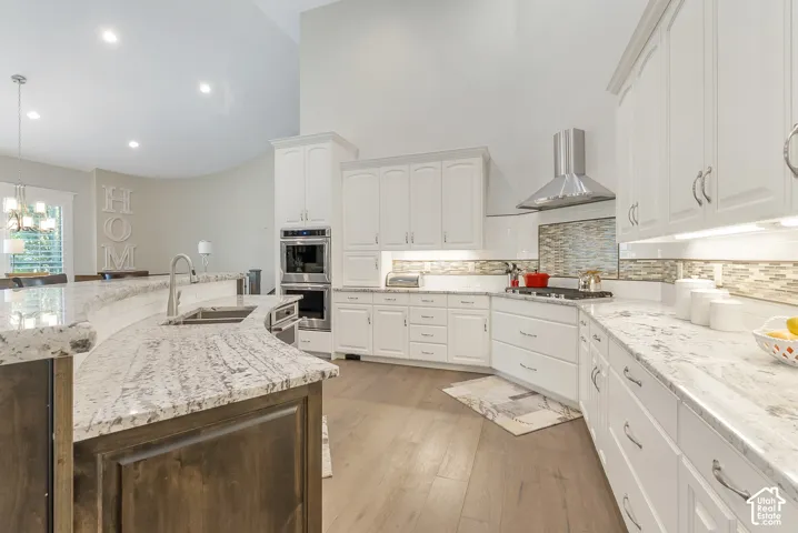 White cabinetry with brushed nickel hardware, stainless steel appliances, light wood-finish flooring, and a stone-finish backsplash