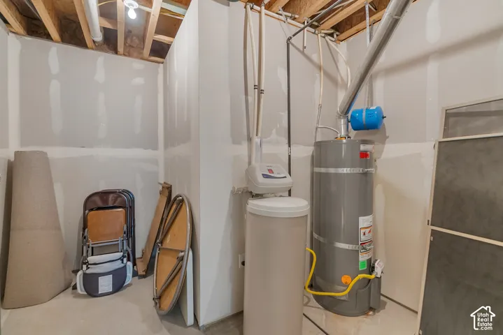 Unfinished space featuring exposed ceiling joists, a water heater, and a water softener system