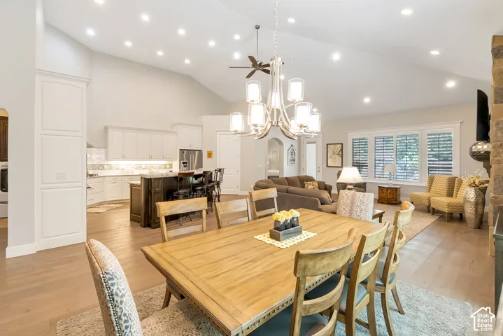 Vaulted ceilings with recessed lighting, wood-finish flooring, white kitchen cabinetry, a kitchen island with seating, and a stone-clad fireplace
