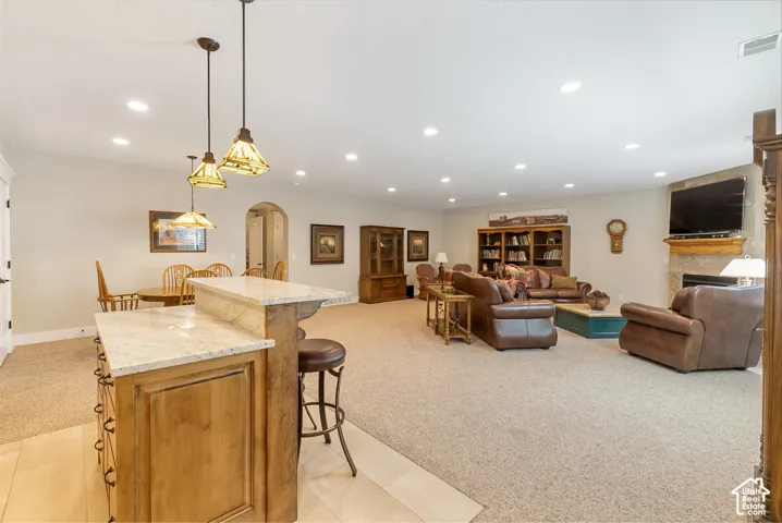 Open-concept recreation area featuring a built-in bar with stone countertops, recessed lighting, and a stone-clad fireplace