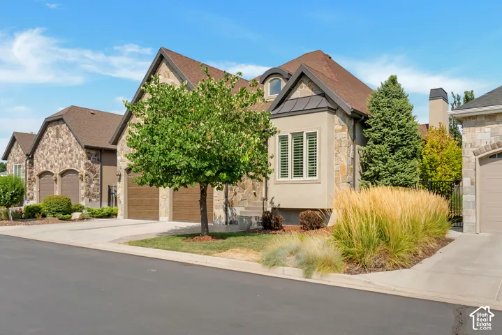Stone facade with dormer window and stucco accents, featuring a two-car garage with wood-finish doors, and a concrete driveway