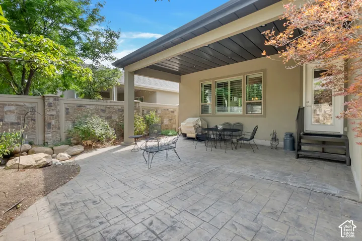 Covered patio with stamped concrete flooring, stone wall, and exterior access