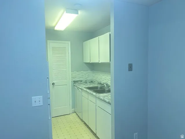 Galley kitchen featuring white cabinetry, dual basin stainless steel sink, patterned countertop, and a tiled backsplash