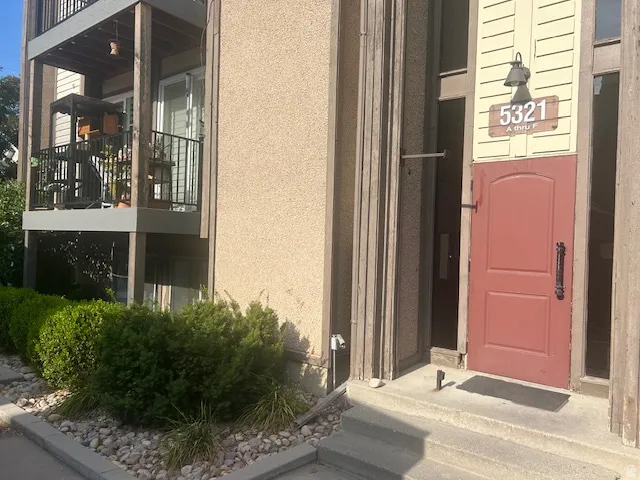 Front entry featuring a red panel door with black hardware, exterior wall lantern, and concrete steps