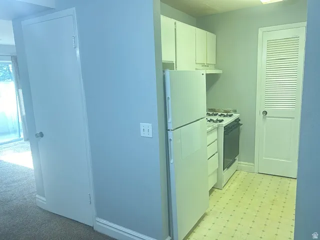 Compact kitchen with white cabinetry, gas range, refrigerator, and patterned floor